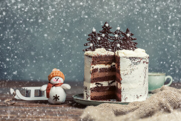 Christmas background with homemade Christmas cake with chocolate Christmas trees and snowman with sled on wooden table.