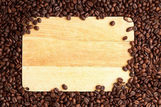 Top view of roasted coffee beans texture background on flat lay in horizontal with wooden board (cutting board) free space in center. pattern for design menu drink. coffee beans frame.