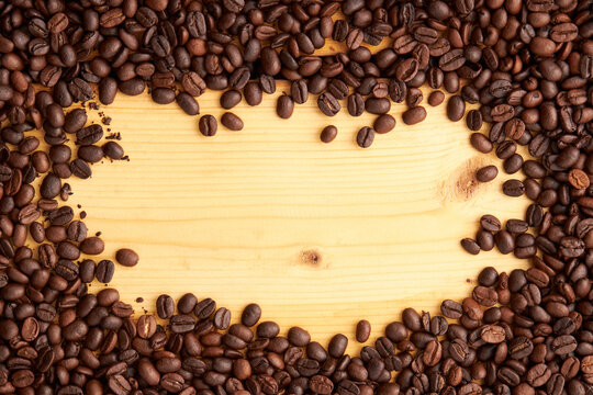 Top view of roasted coffee beans texture background on flat lay in horizontal with wooden board free space in center. pattern for design menu drink. coffee beans frame.