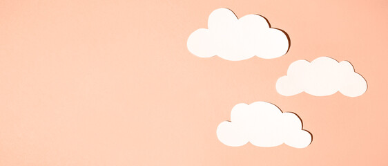 Silhouettes of clouds from white paper on a background. Banner, flat lay, place for text. Peach...