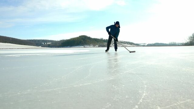 An elderly man practices stricking the puck with hockey sticks on a frozen lake in winter.