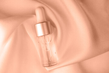 Glass bottle with cosmetic liquid on silk fabric. Peach fuzz is color of year 2024.