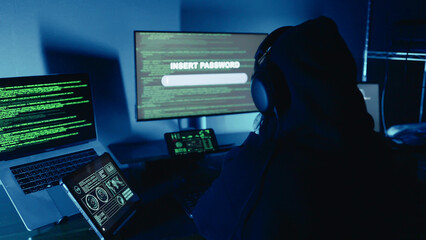 A dangerous hacker in hood and wearing headphones typing security password for login breaks into...