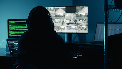 A hacker breaks into company data servers in dark atmosphere and has multiple displays. Hacker in dark room surrounded computers. Hacker breaks into corporate data server. Digital system security