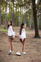 Full length image of a cute two sisters walking in the park, holding hands., behind tree background.