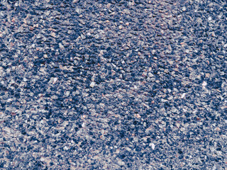 Close-up shot of a textured surface made up of small pebbles in various shades of blue, gray, and pink. Captured from a top-down perspective.