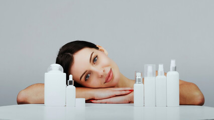 Tender attractive brunette model on a light background near hair and skin care products. The...