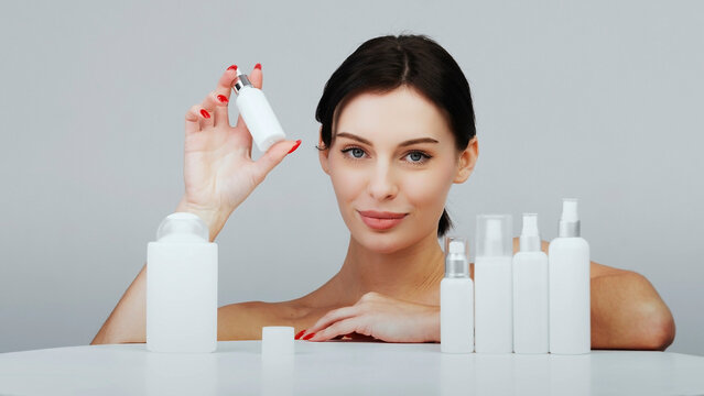 Tender attractive brunette model on a light background near hair and skin care products. The concept of advertising natural cosmetic products and healthy, smooth skin.