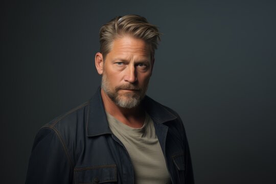 Portrait of a handsome middle-aged man with grey hair and beard in a denim jacket on a dark background
