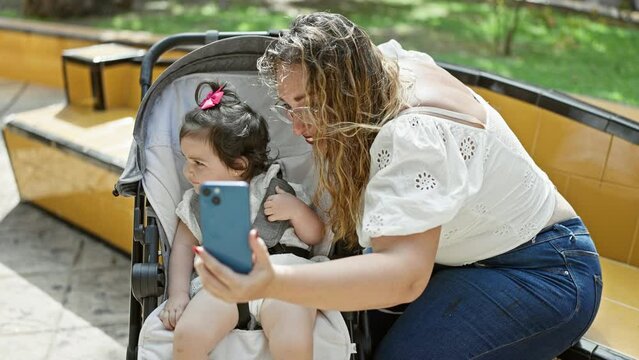 Confident mother and daughter, all smiles, making a fun-filled selfie with smartphone at the park, enjoy a casual day outdoors.