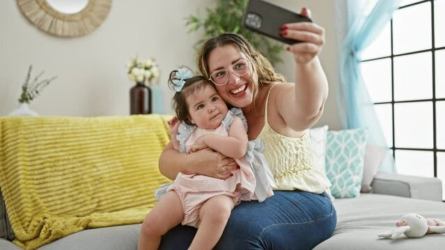Smiling mother and daughter enjoy making fun selfie sittting on sofa at home