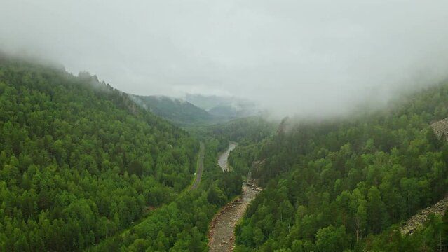 Aerial view of beautiful river among green forest with low foggy clouds. Inzer river in Beloretsk district of Bashkortostan. Fog in a green valley