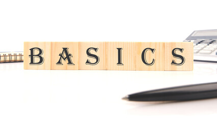 BASICS word word assembled from wooden cubes next to a calculator, pen and notepad