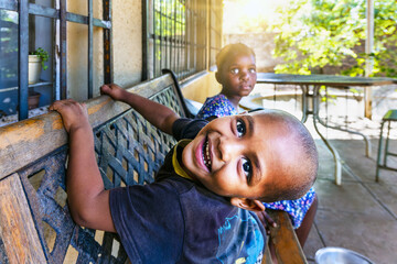 mixed race boy resting on an forged iron bench in front of the house in the favela, playing with...