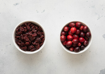 Two bowls with dried red cranberry with ripe cranberries on light background.Top view.