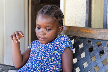 african girl with braids playing on an forged iron bench in front of the house