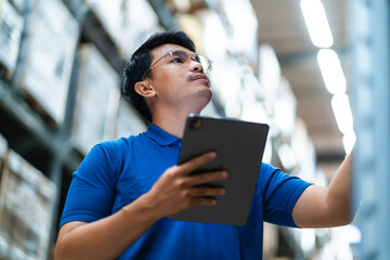 Asian male worker in security suit with tablet computer looking for items in a large warehouse....