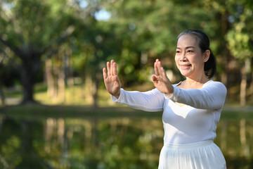 Portrait of mindful senior woman practicing Tai Chi outdoor near lake at summer park