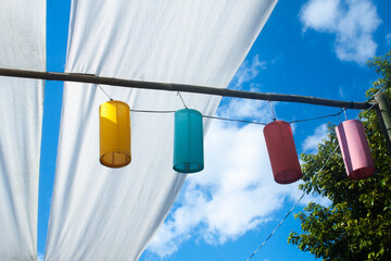 Colorful cylindrical lamps. Hanging on the blue sky background