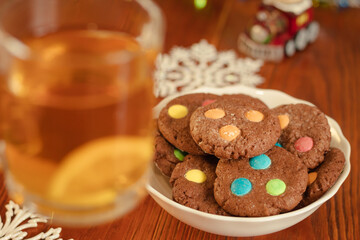 Tea in a cup with lemon. Brown shortbread cookies with jelly beans. Sweet snack in the home kitchen. Selective focus. Wooden background in background and bokeh. Homemade cakes in a white plate