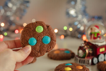 Sweet cookies with colored candies in a woman's hand. Blurred bokeh background. A bright and festive atmosphere in the kitchen at home.