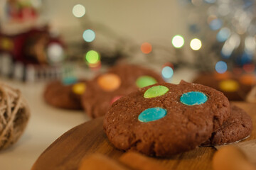 Preparing for the Christmas holidays. Sweet and tasty brown cookies with bright candies. Background with blurred bokeh from garland and tinsel.