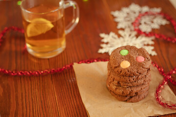 Brown cookies with colored candies and tea with lemon next to it on a wooden table. Breakfast in a cafe. New Year's sweet pastries.