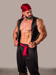 A muscular topless man with a red bandanna and pirate costume, standing in front of a white background. A Brave Soul in Crimson: A Male Bodybuilder with a Red Bandanna Standing Proudly Before a Clean