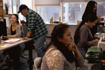 man checking his colleague's work in the office. male controlling his assistant. businessman holding a glass of tea teaching a new coworker. working women in the foregroundof the photo