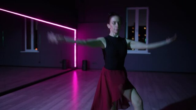 Live camera. An elegant arabesque performed by a beautiful ballerina in a dark choreographic hall with neon lighting