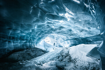 Landscape view of a hiker contemplating a beautiful blue textured ice cave in the Furgg glacier in...