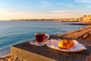 concept of street outdoor breakfast with a cup of tea or coffee on a morning coast during sunrise. landscape of city embarkment with sea water and cloudy sky on background
