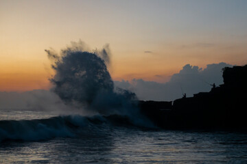 Sunset at Balinese coast, Indonesia, silhouette of fishermen in front of giant waves