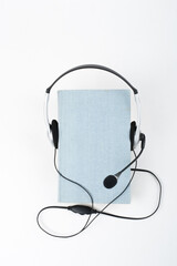 Audiobook on white background. Headphones put over blue hardback book, empty cover, copy space for ad text. Distance education, e-learning concept. Top view