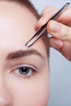 Young woman with short hair plucking eyebrows tweezers close up