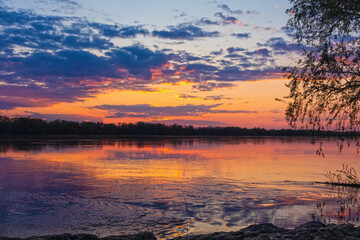 Sunset landscape over a wide river in the countryside. Sunlight illuminates the clouds in the evening sky