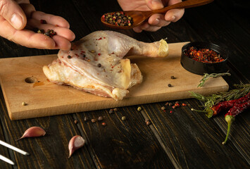 Cooking raw chicken leg on a kitchen cutting board. Adding pepper by hand and spoon to chicken leg before grilling