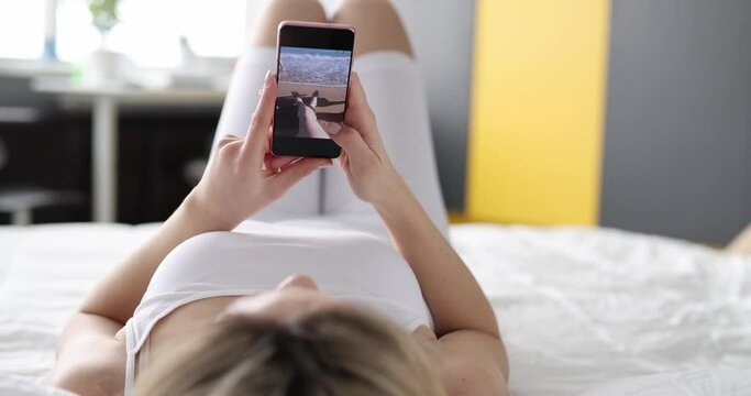 Woman using modern smartphone looks through photos from relaxing on bed at home closeup. Memories from travel concept
