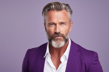 Portrait of mature man with beard and mustache looking at camera while standing against purple...