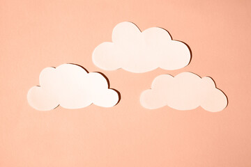 Silhouettes of clouds from white paper. Banner, flat lay, place for text. Peach fuzz is color of year 2024.