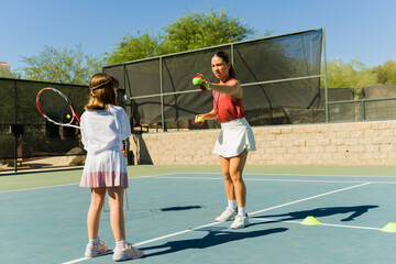 Naklejka premium Adorable girl kid at tennis school practicing with a trainer