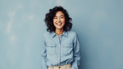 Beautiful attractive Asian female with casual jean smile cheerful standing against plain background peach color, young happy student or worker woman soft skin charming face with long curly hairstyle
