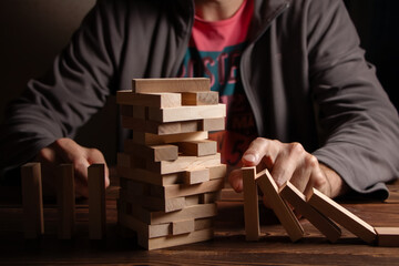 Man's fingers prevent the wooden block game stick from falling domino - obrazy, fototapety, plakaty