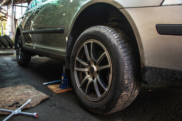 Car lifted by scissor jack without wheel outdoors, closeup. Tire puncture