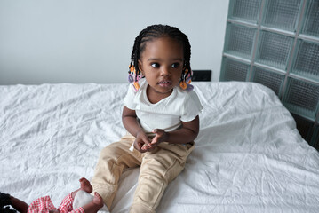 cute nice little African American girl sitting on white bed. close up photo. happy childhood, beauty