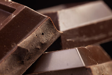 Broken chocolate. Chocolate pieces. Chocolate pieces on dark background.