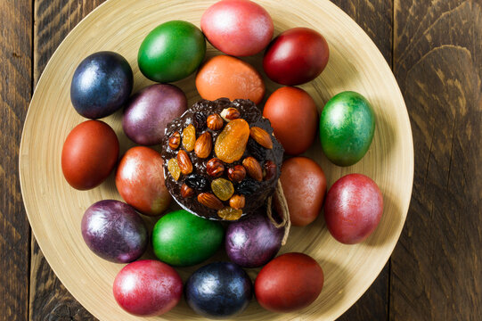 a large wooden plate with an Easter cake and flowered eggs on a rustic wooden table. top view. close angle.