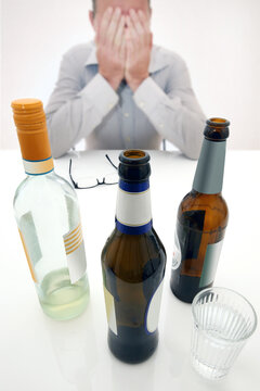 Männlicher Alkoholiker mit Wein- und Bierflaschen sitzt in verzweifelter Pose am Tisch