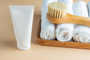 Fototapeta na wymiar SPA cosmetics, woman body and skincare products on wooden tray on beige background. Natural bristle dry massage brush and body or face cream in white plastic tube.