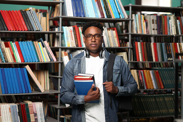 Young black man in a white T-shirt and denim jacket looks thoughtfully at the camera, with a stack...